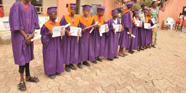 Élèves en toge et toque violettes, diplôme en main, dans la cour de l'école
