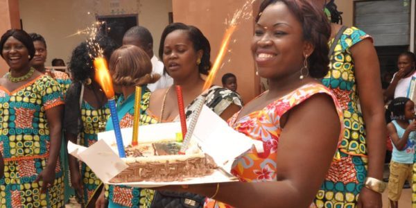 Une femme présente un gâteau orné de bougies étincelantes, entourée de personnes en tenues colorées